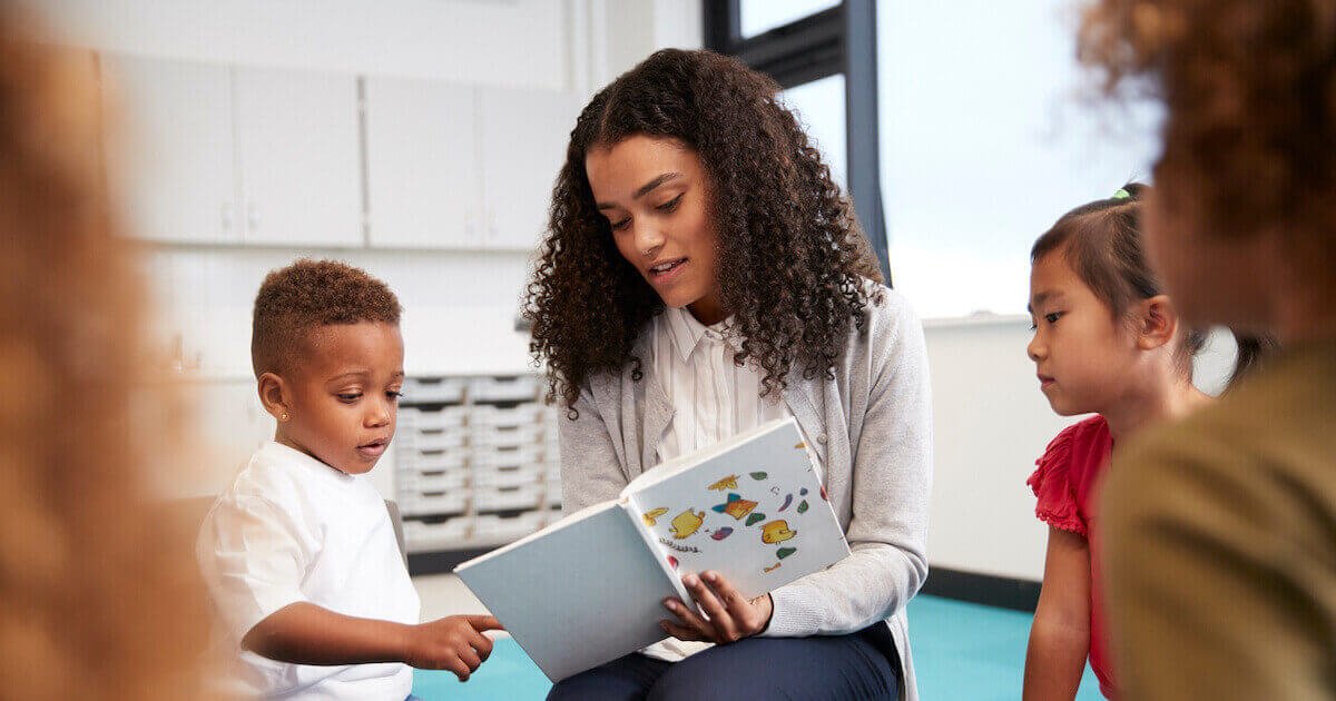 A teacher engages students by reading a story in a classroom, promoting teacher-centered learning and student interaction.