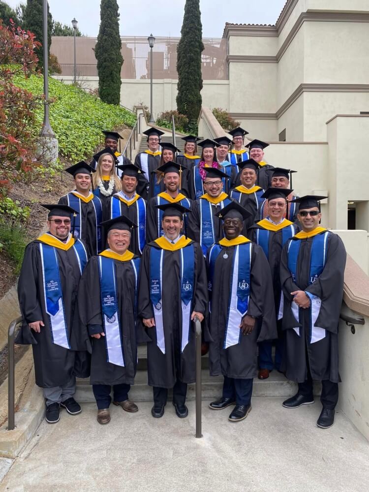 a group of students and teachers pose together in caps and gowns after a graduation ceremony for cyber security operations leadership