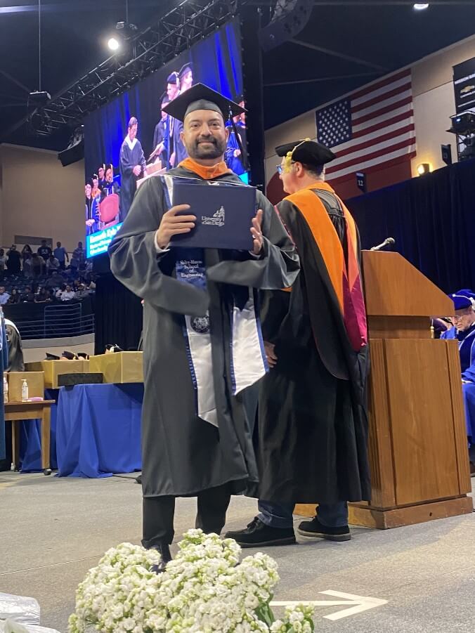 a gradute of the cyber security engineering program stands on stage with their diploma in hand during the ceremony