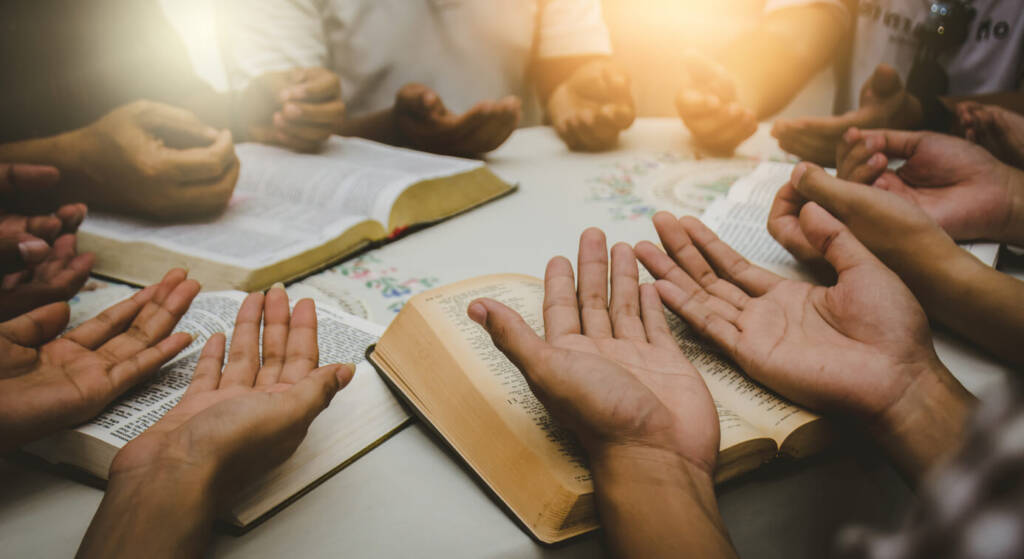 a group of people sit around a table with their hands on religious books, palms facing upwards