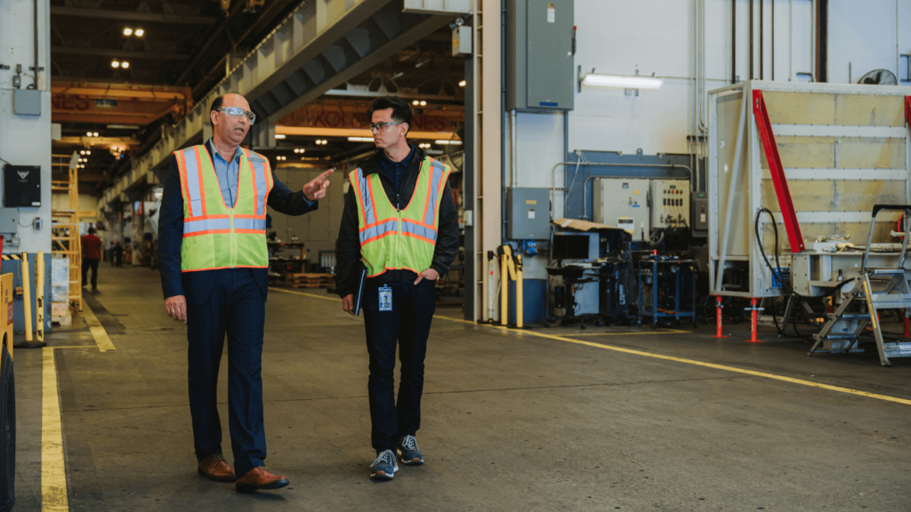 two engineers with reflective vests walking side by side in a warehouse.