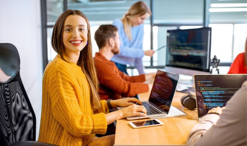 Team of a young woman as a programmer sitting in the office with people working on the background