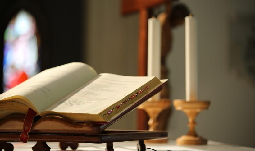 an open bible sits on a podium with two large white candles in the background