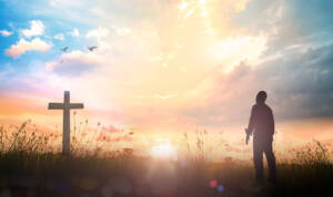 man standing by cross at sunset