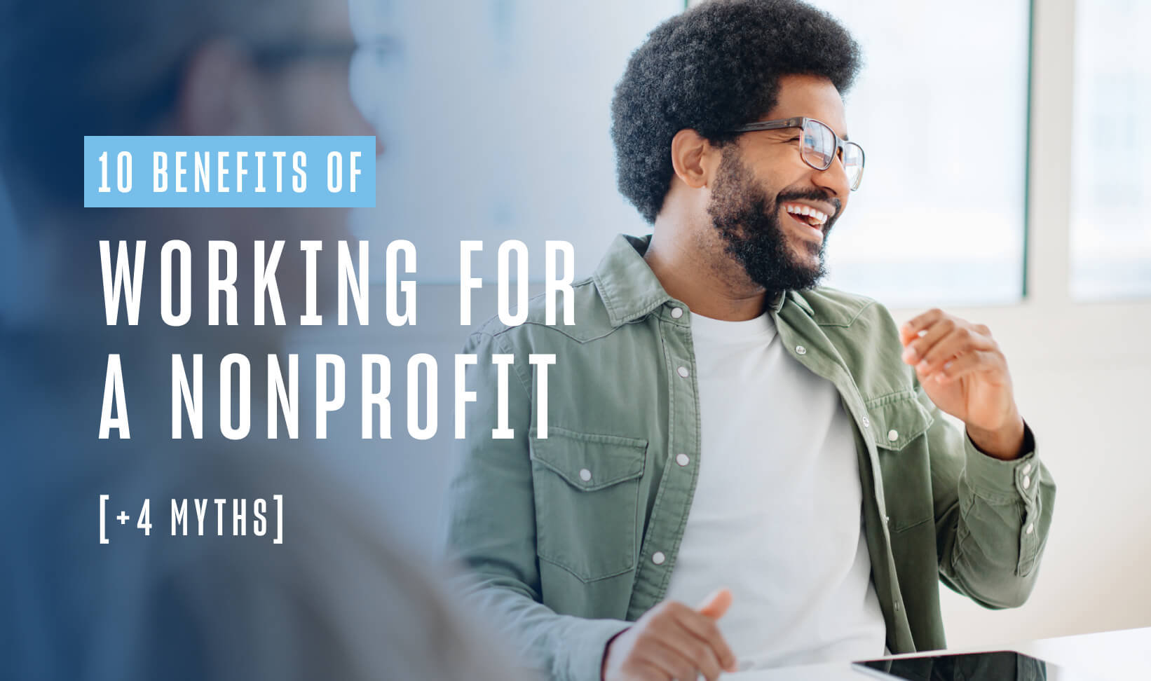 man with black hair and a black beard wearing 10 Benefits of Working for a Nonprofit [+ 4 Myths] | glasses and a green button down shirt sits at a table, smiling
