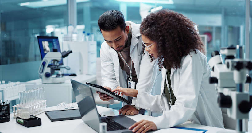 Two scientists in lab coats studying a laptop screen intently.