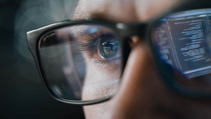 A man with glasses focused on a computer screen.