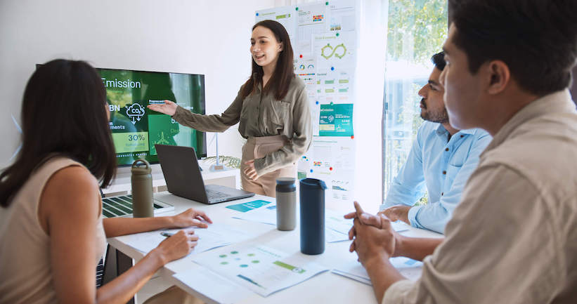 A woman presents to an audience, engaging them with her speech and visual aids in a professional setting.