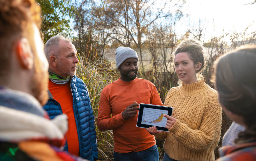 A diverse group of individuals gathered around a tablet, engaged in discussion and sharing ideas.