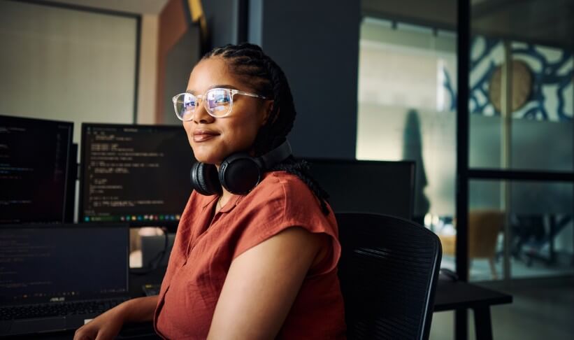 Young woman programmer focused on her work, coding on dual monitors in a modern office environment