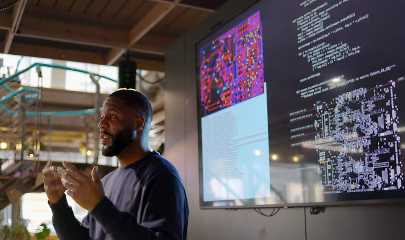 man talking with his back turned to a big screen