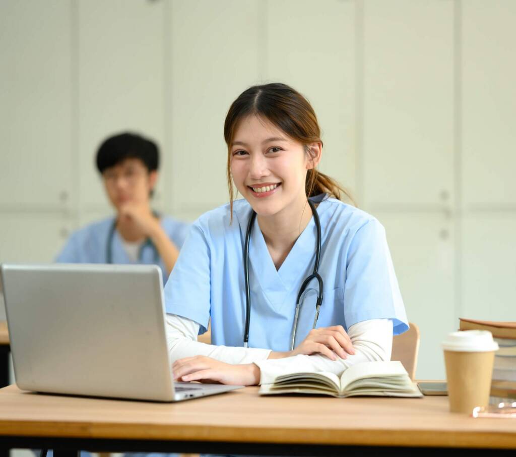Nurse in scrubs sitting at a desk looking at a laptop