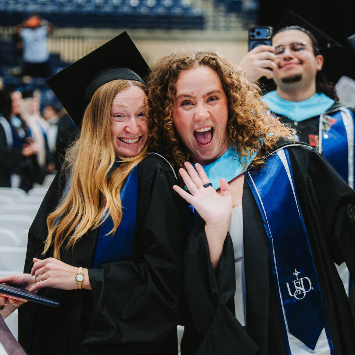 Two women smiling and waiving in graduation gown at USD commencement
